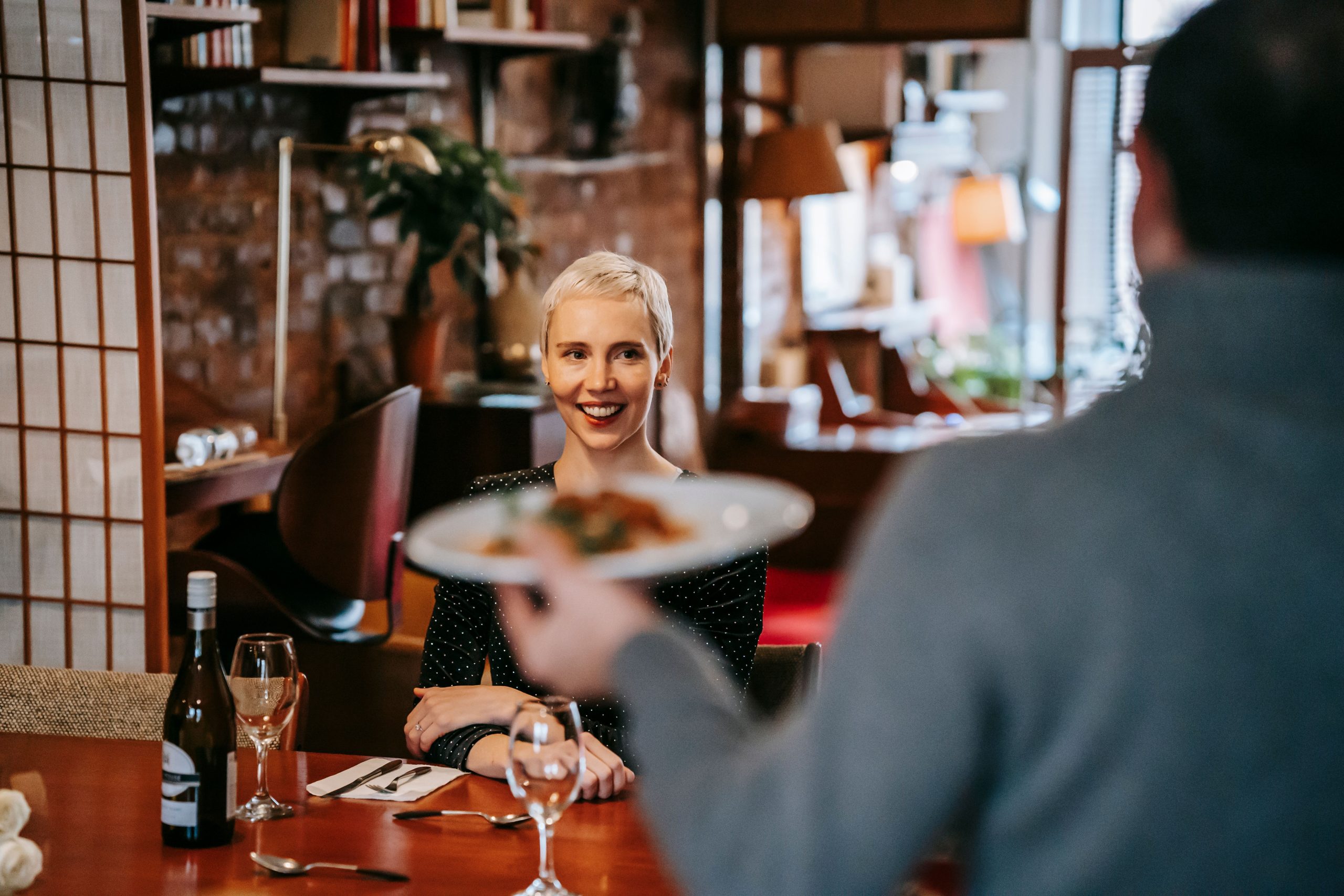 Couple on a dinner date at a bright restaurant, man serving wine to woman at table
