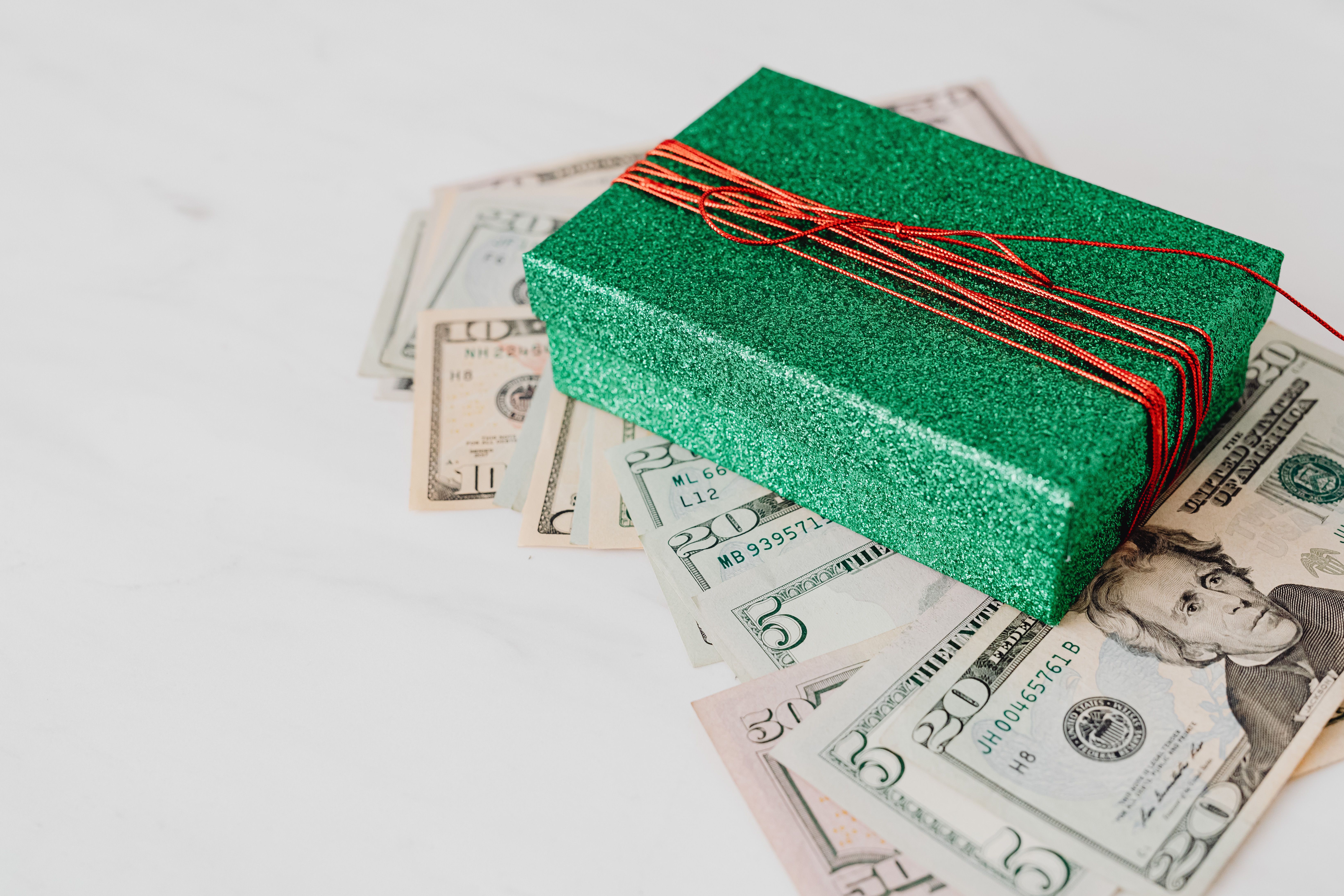 Sparkling green gift box sitting atop scattered US dollar bills symbolizing wealth and generosity