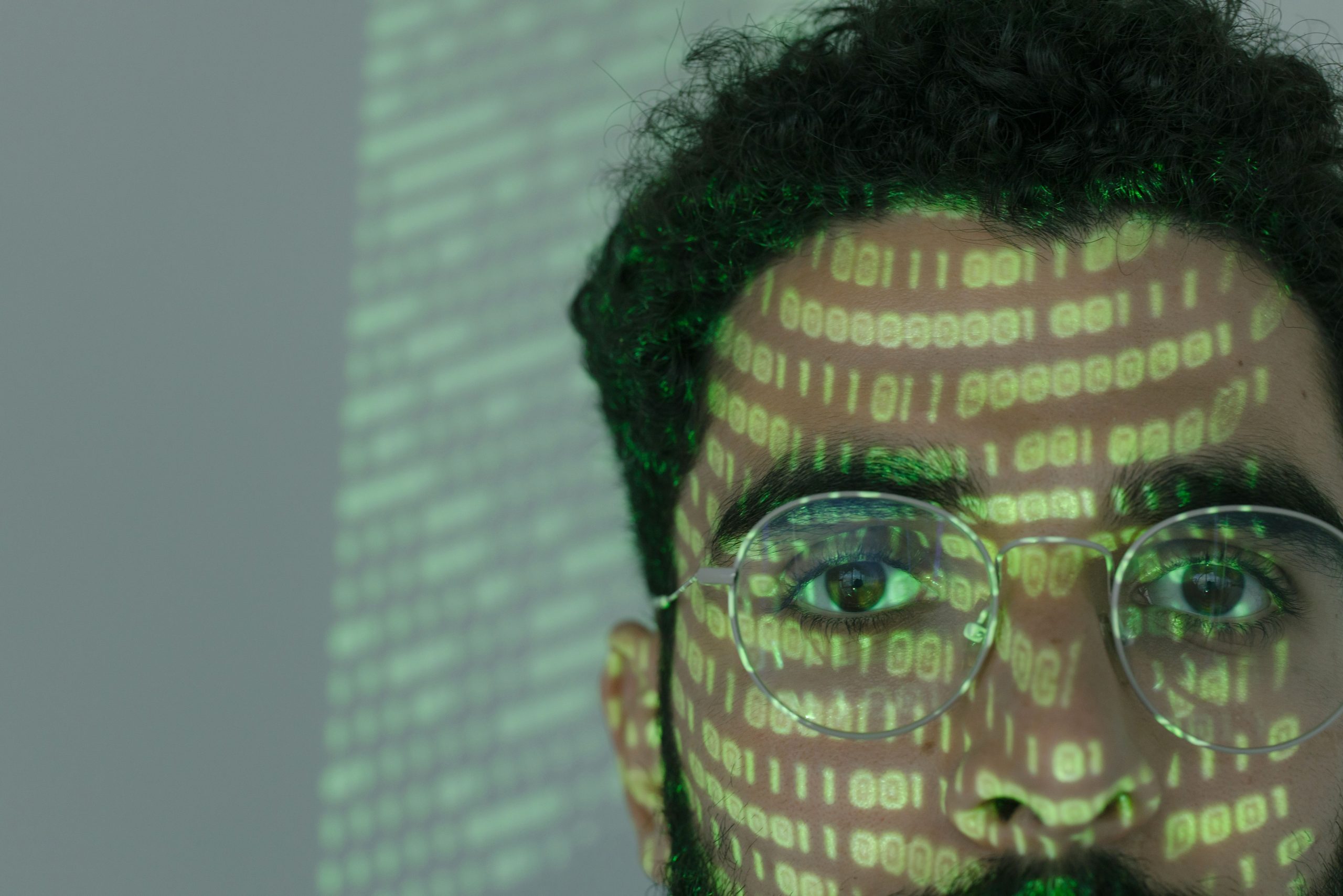 Close-up of a man's face with binary code projected across it, illustrating deepfake AI face manipulation