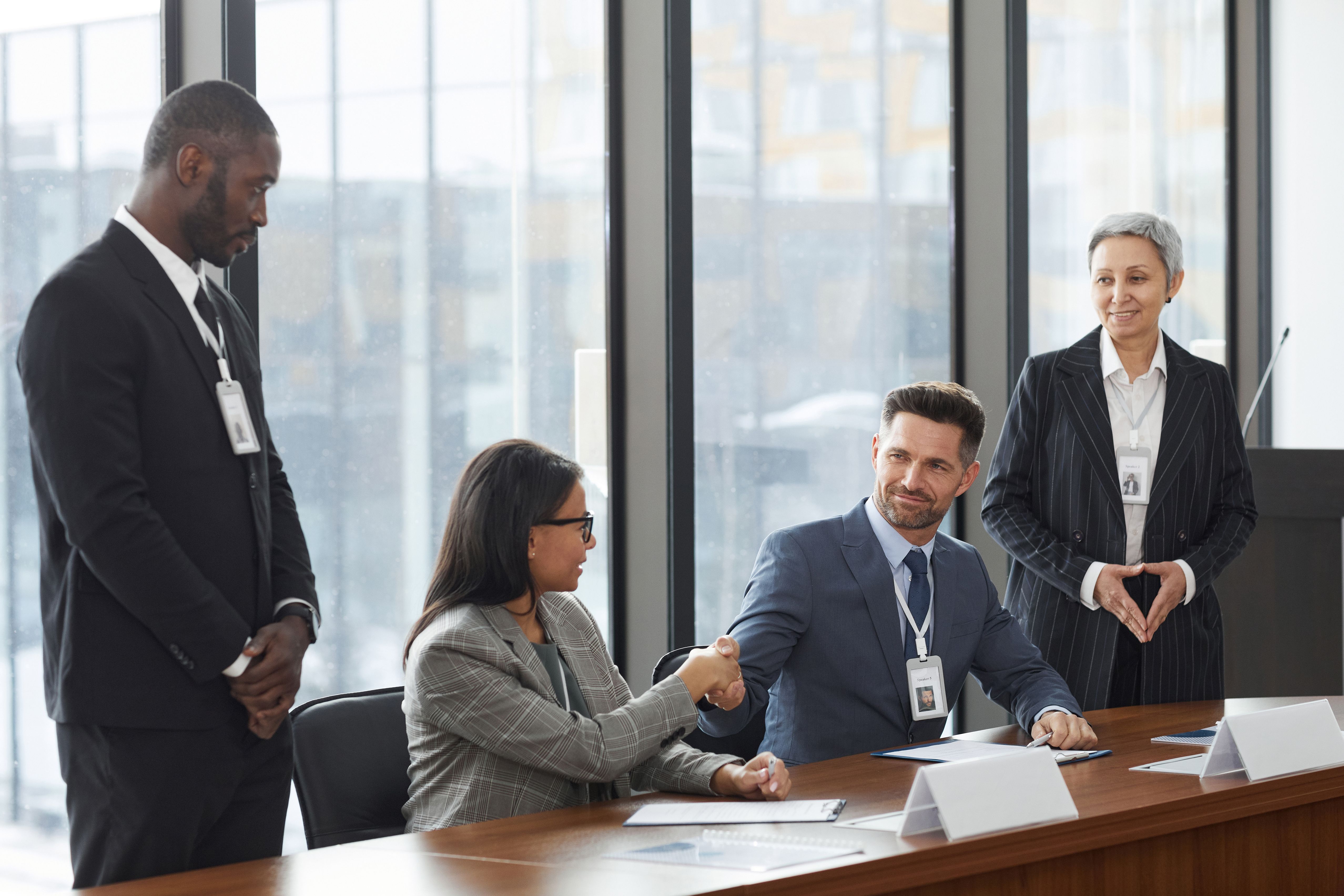 Diverse professionals shaking hands during a business meeting, representing a leadership handover