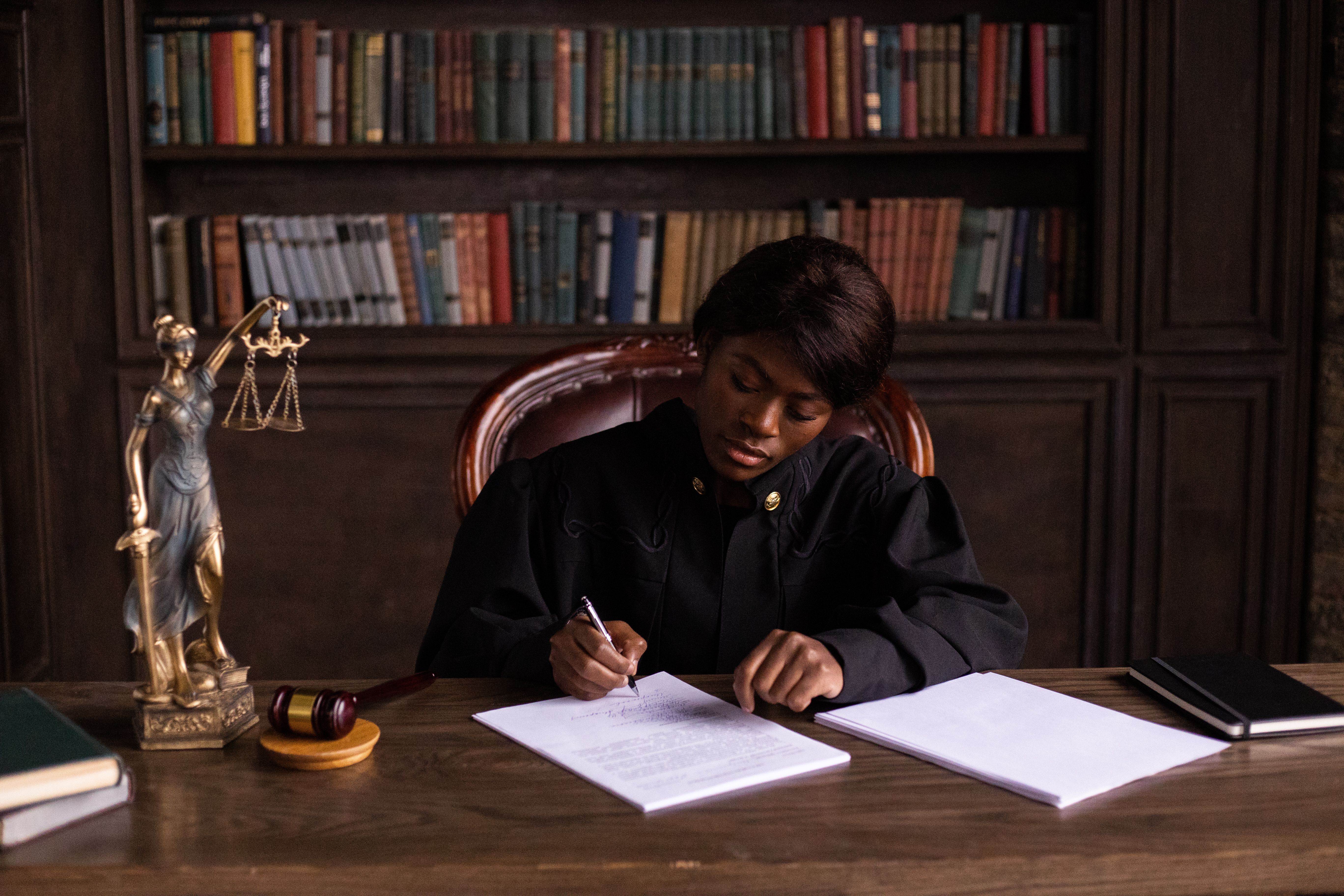 Judge writing on a legal document beside shelves of law books
