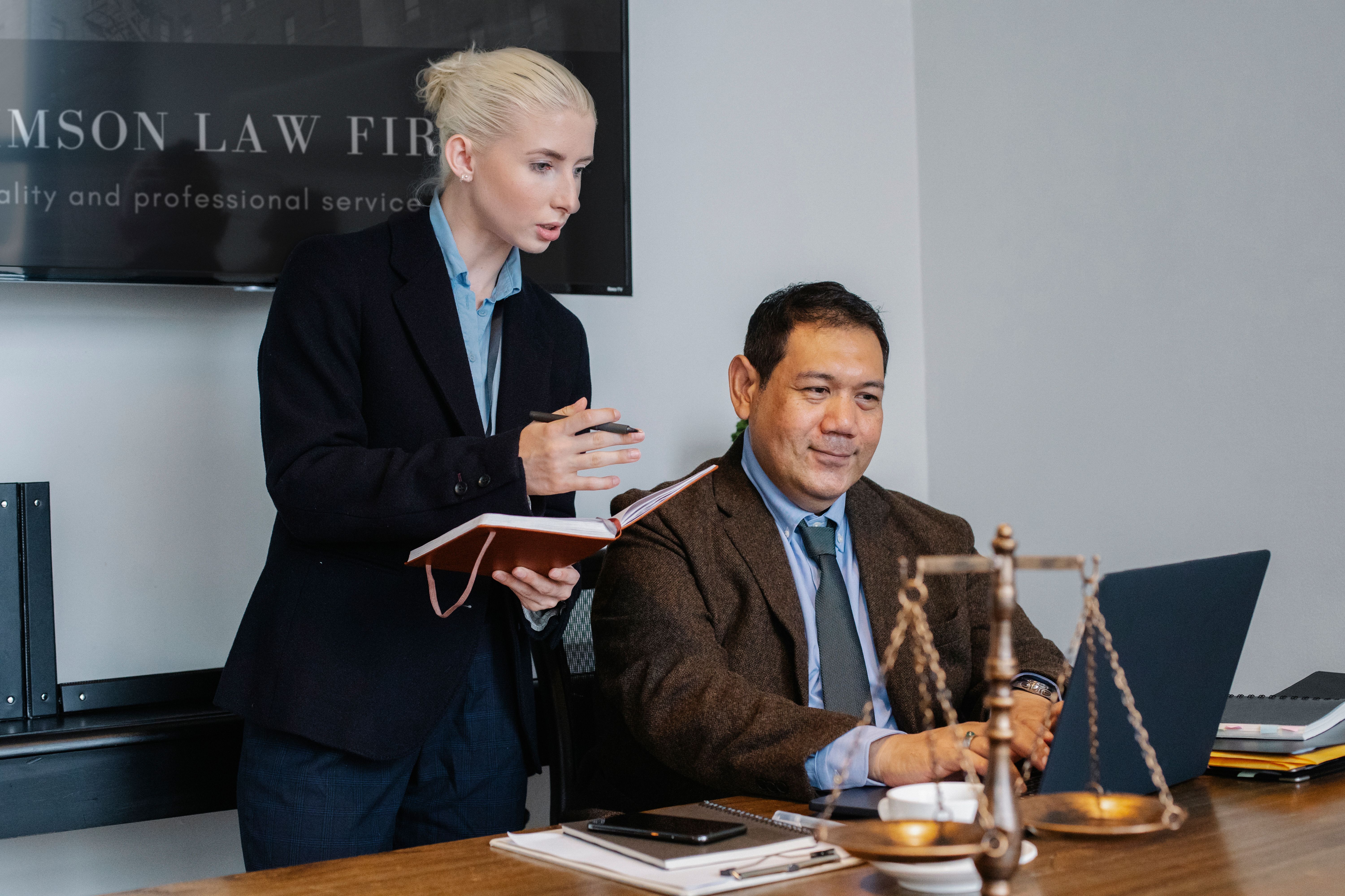 Legal assistant taking notes beside a colleague working at a laptop