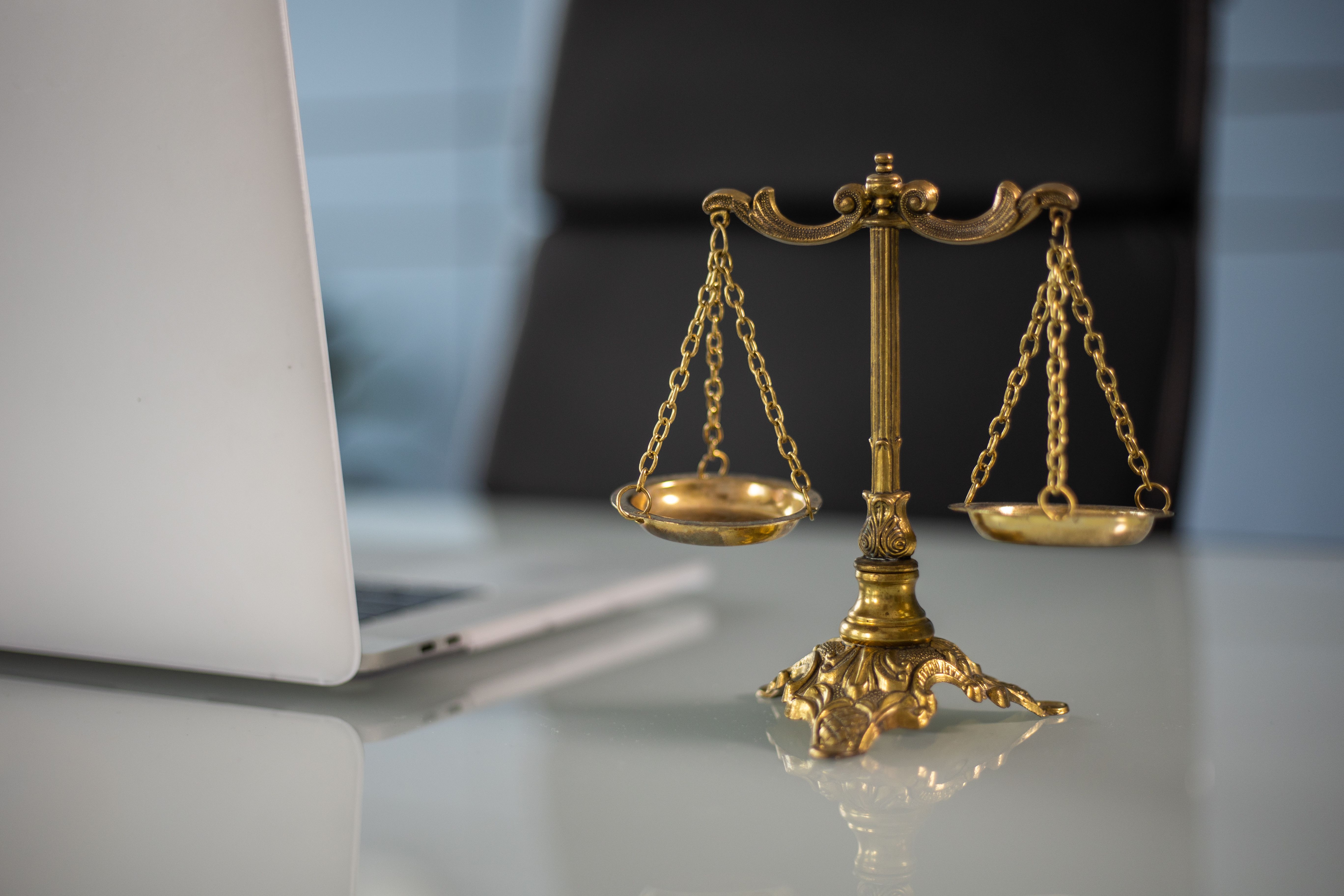 Golden scales of justice on a desk beside a laptop, symbolizing legal balance and oversight